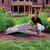 A woman lifting the DekoRRa Model 112 fake rock cover to reveal a green septic riser, demonstrating its lightweight yet durable design in a landscaped yard. View Product Image