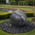 Black and gray granite sphere water fountain with natural stone veining, water bubbling from the top, set on dark river rocks in a landscaped lawn. View Product Image