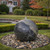 Black and gray granite sphere fountain with marbled stone texture, water bubbling from the top, displayed on mixed river pebbles in a landscaped yard. View Product Image