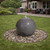 Polished granite sphere fountain with water bubbling over the top, set in black river stones on green lawn with backyard pool, patio chairs, and shed. View Product Image