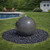 Dark granite sphere fountain bubbling gently, set in black river stones on green lawn, with backyard pool, patio seating, and garden shed. View Product Image