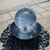 Overhead view of a Blue Thumb 14-inch crystal sphere fountain with water flowing evenly over the acrylic surface, surrounded by black polished pebbles. View Product Image