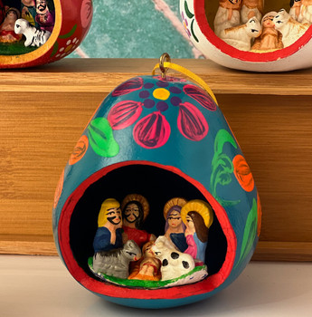 Close-up of a handmade Peruvian gourd nativity showing detailed clay figures of the Holy Family in a tiny painted creche, Fair Trade Christmas decor.