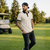 Man walking on a golf course wearing a striped polo shirt and cap.