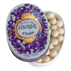 Tin of Violet Anis de Flavigny candies surrounded by delicate violet blossoms, evoking the floral aroma and traditional charm of this classic French confection.