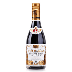 The image showcases a bottle of Giuseppe Giusti Aceto Balsamico di Modena. The bottle is tall and slender with a golden cap, which adds a touch of sophistication. The label is quite ornate, featuring a white background with a classic, elegant script and decorative elements in black and gold that convey a sense of luxury and tradition.

At the very top, just below the cap, is a small, oval label with a red background featuring the Giusti family crest – a white cross – and the name "GIUSTI" in white lettering, denoting the esteemed brand. The main label below has "ACETO BALSAMICO DI MODENA" in prominent, bold letters, clearly stating what the product is. Beneath this, "GIUSEPPE GIUSTI" is written, linking the product directly to its historic producer.

Other decorative and text elements likely include details about the balsamic vinegar's age, quality, and perhaps its heritage. The overall impression given by the bottle is that of a high-end, traditionally made balsamic vinegar that is rooted in Italian culinary culture.