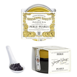 The image displays a product by Giuseppe Giusti named "Perle" or "Pearls", which are small, spherical beads resembling caviar. These pearls are likely a balsamic vinegar product made using a molecular gastronomy technique known as spherification. The packaging is elegant, with a predominantly gold and white color scheme that suggests a premium product.

On the left, there is a clear plastic spoon filled with the dark, glossy balsamic pearls, showing the product itself. In the center, the front of the package features a label with the text "Gran Deposito Giuseppe Giusti Modena" around the top, indicating the heritage and quality of the product. The word "Perle - Pearls" is in the center in bold, with additional text likely describing the product as balsamic pearls.

On the right, we see the side of the same packaging, maintaining the color scheme and elegance, with the Giusti branding more minimal here, focused on the product name "PERLE". The overall image communicates a gourmet product likely used for garnishing and adding a sophisticated touch to dishes.
