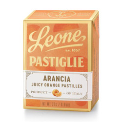 The image is of a "Leone Pastiglie" box, which contains juicy orange pastilles. The packaging design has a warm orange color palette that suggests the flavor of the candies. At the top, the name "Leone" is featured prominently with the foundation date "dal 1857" indicating the brand's long history. The word "Pastiglie" is elegantly scripted across the center. The label on the lower part of the box displays the word "Arancia," which is Italian for orange, and it's followed by "Juicy Orange Pastilles" to describe the product. The white label has a realistic image of an orange slice, emphasizing the flavor. The packaging also states "Product of Italy," denoting its origin, and the net weight is listed as 27g / 0.95oz. The box's design conveys a sense of traditional Italian confectionery.