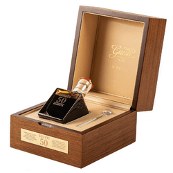 The image showcases a luxurious balsamic vinegar bottle, housed within an elegant wooden presentation box. The bottle is unique, with a square base and an asymmetrical, tilted body design. It features a gold-colored cap and a label indicating that it is a 50-year-old balsamic vinegar from "Giuseppe Giusti." The inside of the box is lined with gold-colored material, and the outside of the box has a gold inscription of the Giusti logo along with a plaque stating "Giusti Balsamico 50 anni." This setup emphasizes the exclusivity and premium quality of the vinegar, suitable for a collector's item or a prestigious gift.