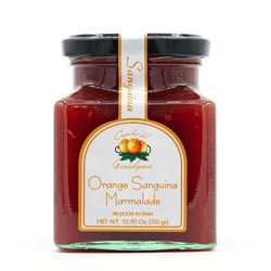 The image displays a jar of Caprichos del Guadalquivir Red Orange Jam (Mermelada de Naranja Sanguina). The jar is square-shaped with a black lid, and it contains a vibrant red jam. The label features the brand name "Caprichos del Guadalquivir" prominently, along with an illustration of two red oranges with green leaves. The word "Sanguina" is printed on a red ribbon that runs vertically from the lid to the label. The label text is primarily in Spanish, highlighting the product as "Mermelada de Naranja," which means "Orange Jam."