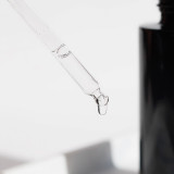 A clear dropper with a droplet of liquid at the tip, positioned near a dark bottle.