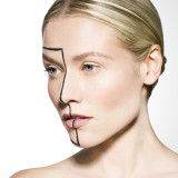 A profile of a woman with a striking black line design on her face, set against a light background.