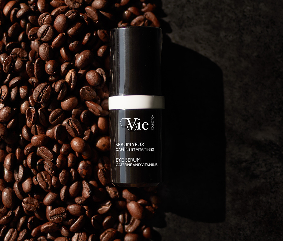 Eye Serum Caffeine and Vitamin, 15 ml pump laying on a table next to a pile of coffee beans.