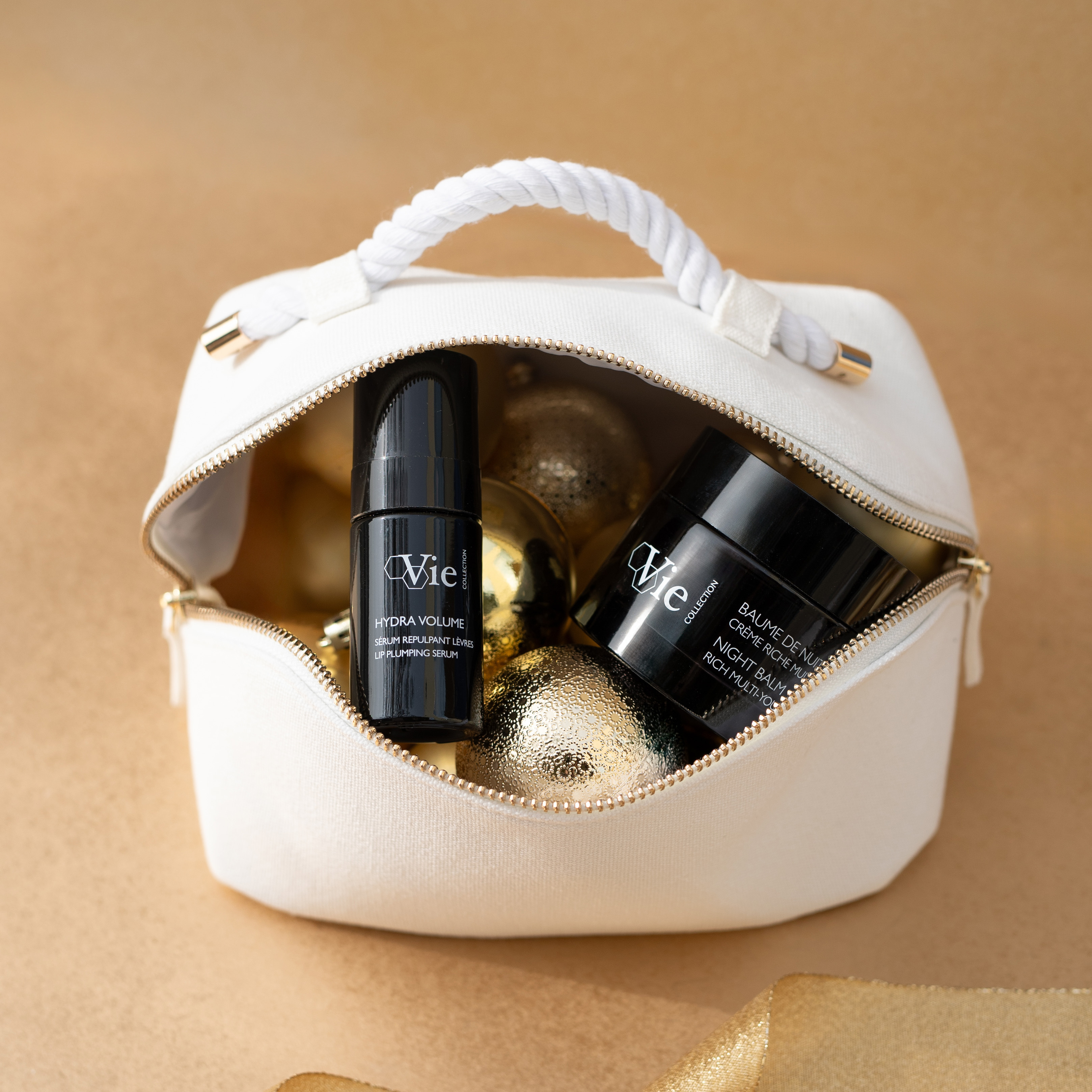 Night Balm Rich Multi-Youth Cream and Hydra Volume Lip Plumping Serum laying together in a white pouch.