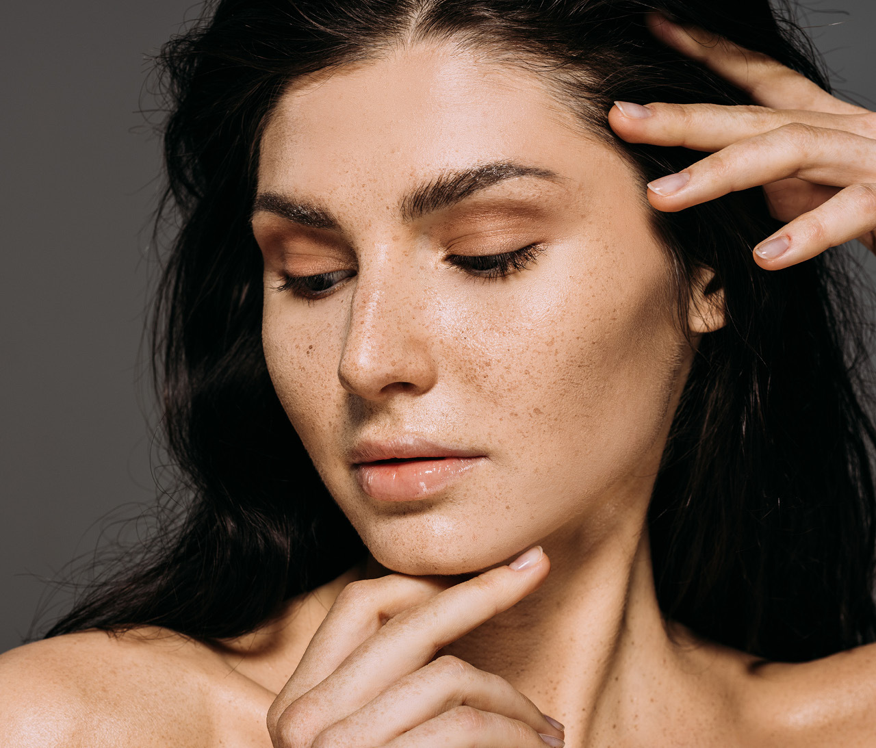 Woman gazing downward, gentle caressing her face