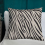 All-over black and cream zebra Napoleon pillow upright on white chair with teal wood paneling.