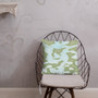 Sage green and aqua camo-style Botticelli Girls pillow on a black wire chair in a bright room.