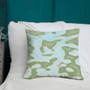 Olive and sky-blue watercolor camo Botticelli Girls pillow leaning on white cushion by teal wall.