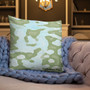 Sage green and pale blue abstract camo Botticelli Girls pillow on beige sofa with periwinkle knit blanket.