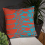 Coral-orange pillow with five teal reclining figure rows on copper wire chair beside houseplant.