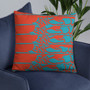 Orange-red pillow with four teal abstract bands on navy velvet chair against grey wall.