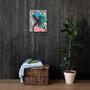Da Vinci teal-pink caricature canvas on dark wood-slat wall above wicker chest and rubber plant.