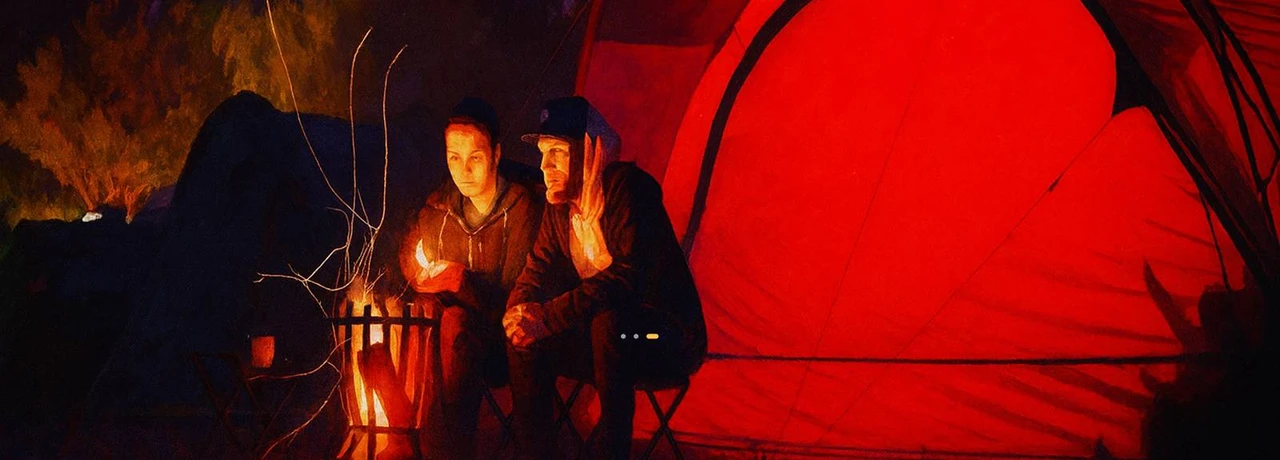 2 people sitting infront of a campfire with a tent behind them