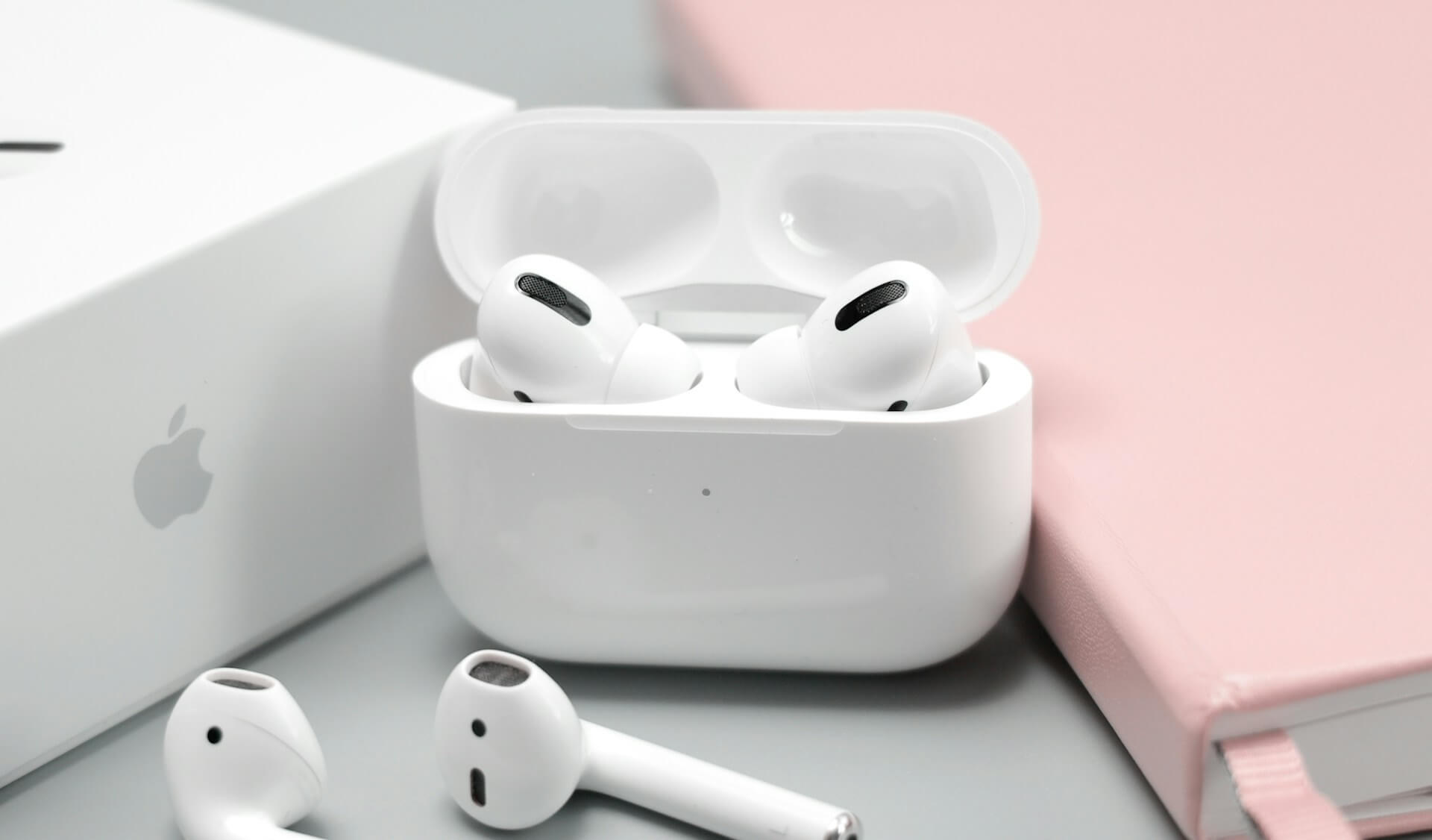 AirPods Pro in case next to AirPods and pink notebook on table