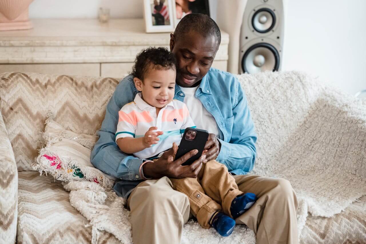 dad sitting on sofa with son and playing with smartphone