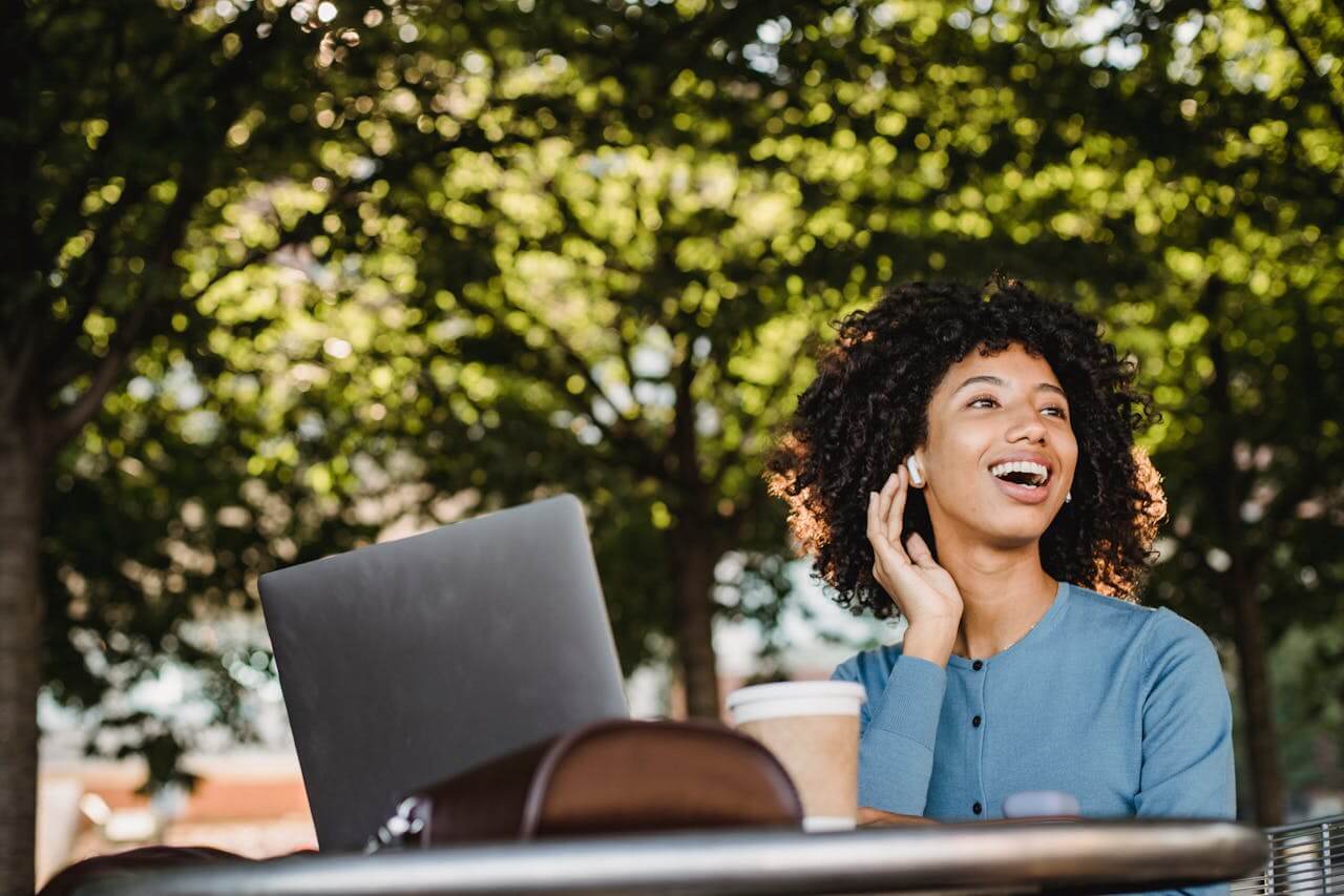 smiling woman with AirPods and laptop on outdoor bench
