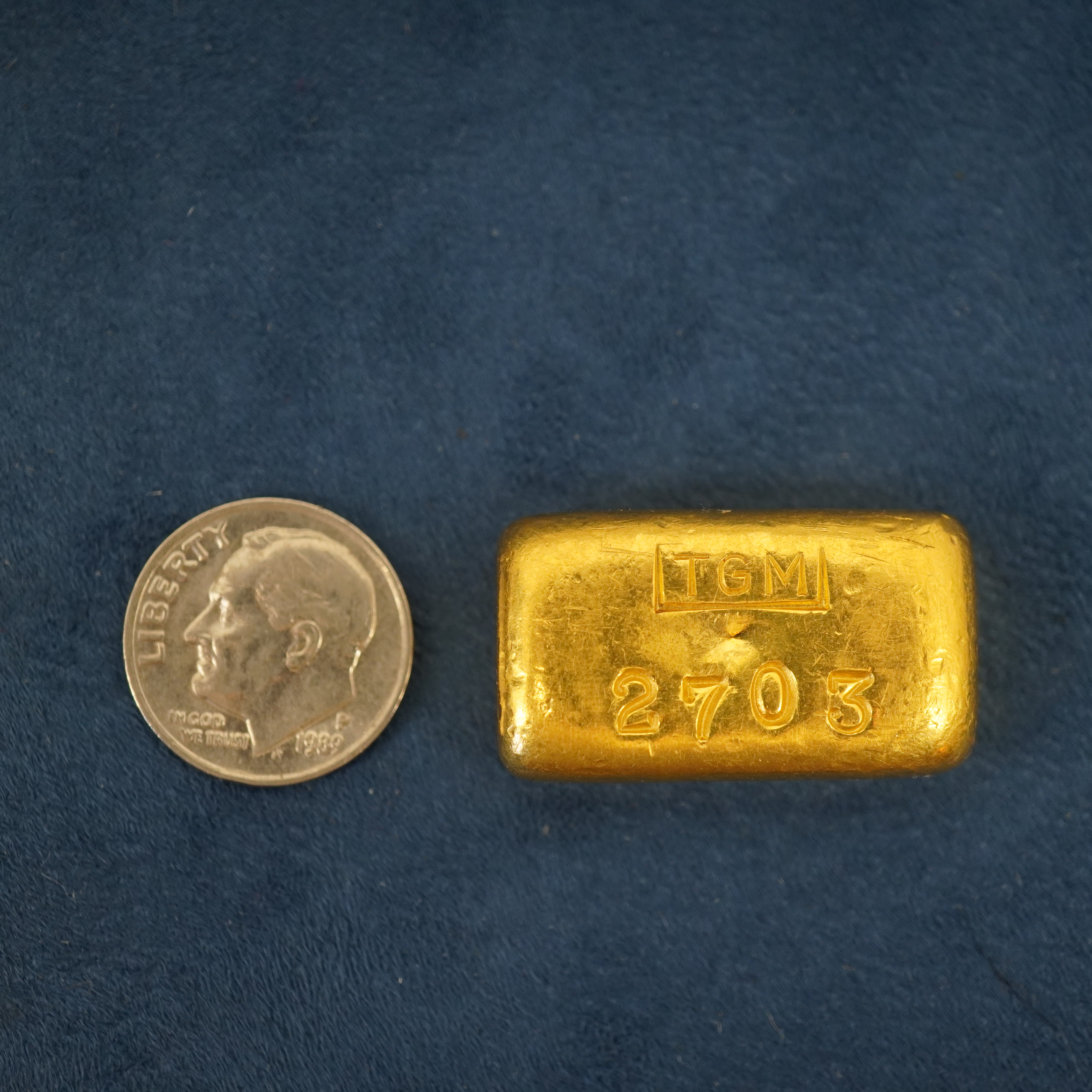 2 troy ounce bar of pure gold next to a dime, showing that they are the same size.