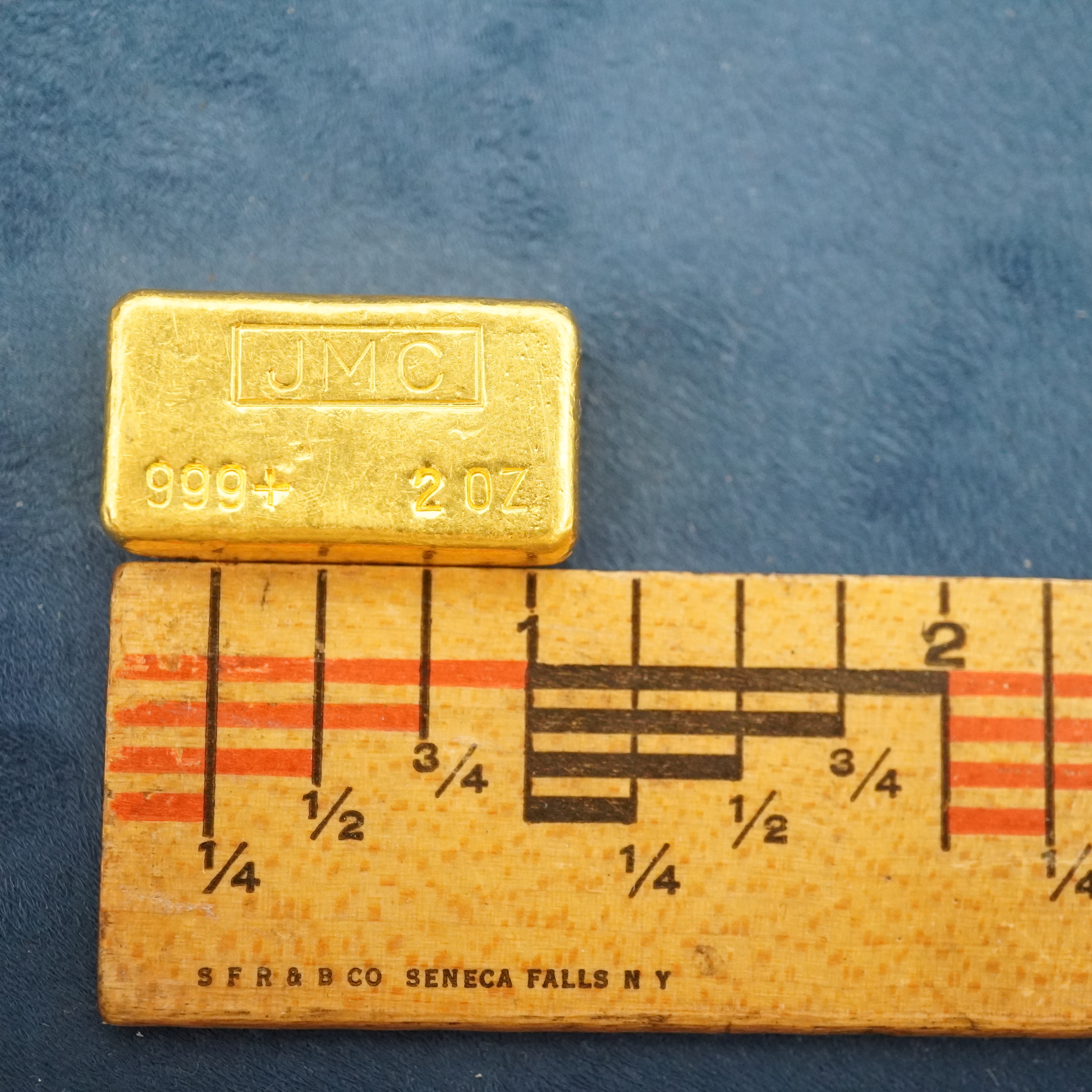 2 troy ounce pure gold bar with a ruler measuring the length of the bar to be about 1 inch.