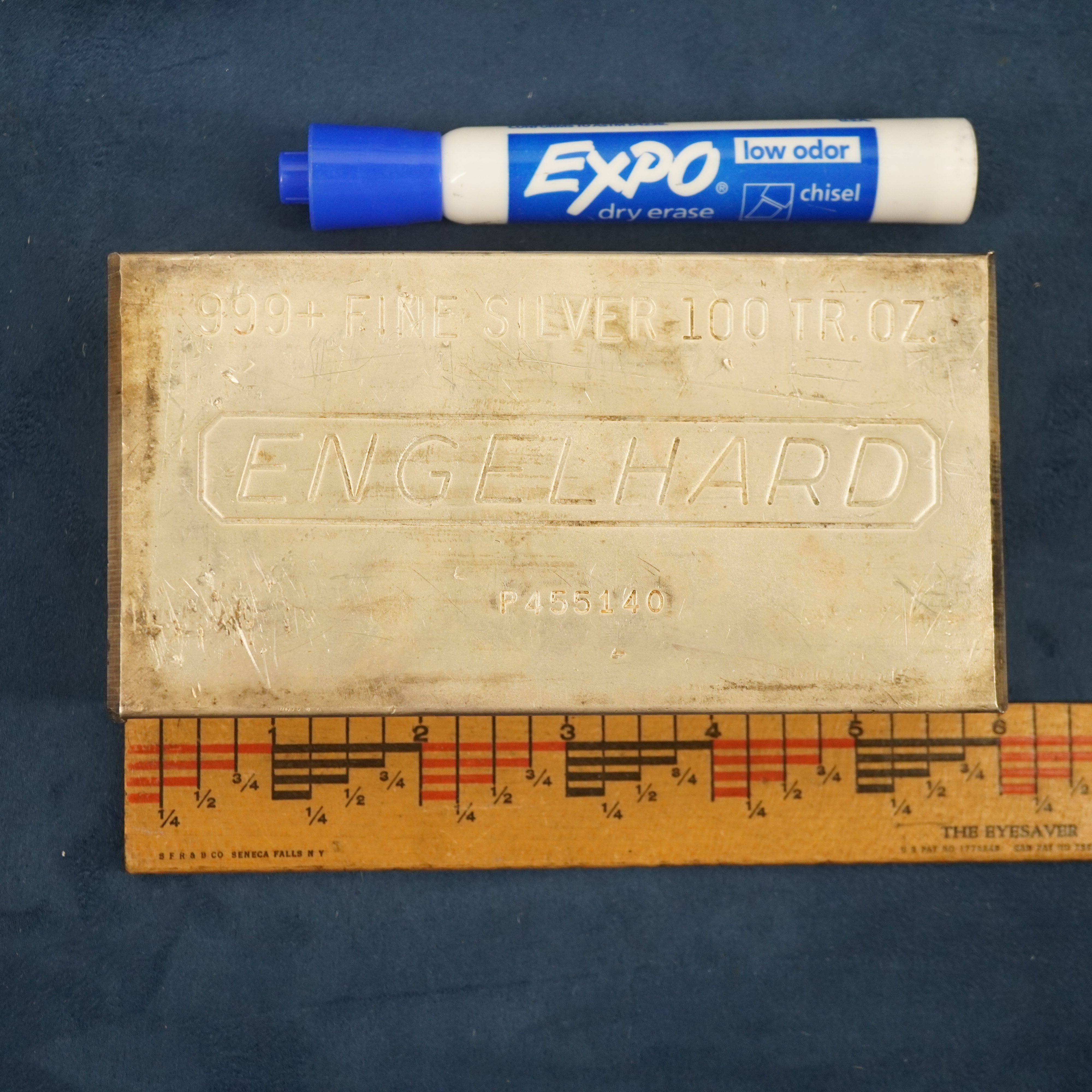 100 troy ounce pure silver bar with a ruler measuring the length of the bar to be 6 inches.