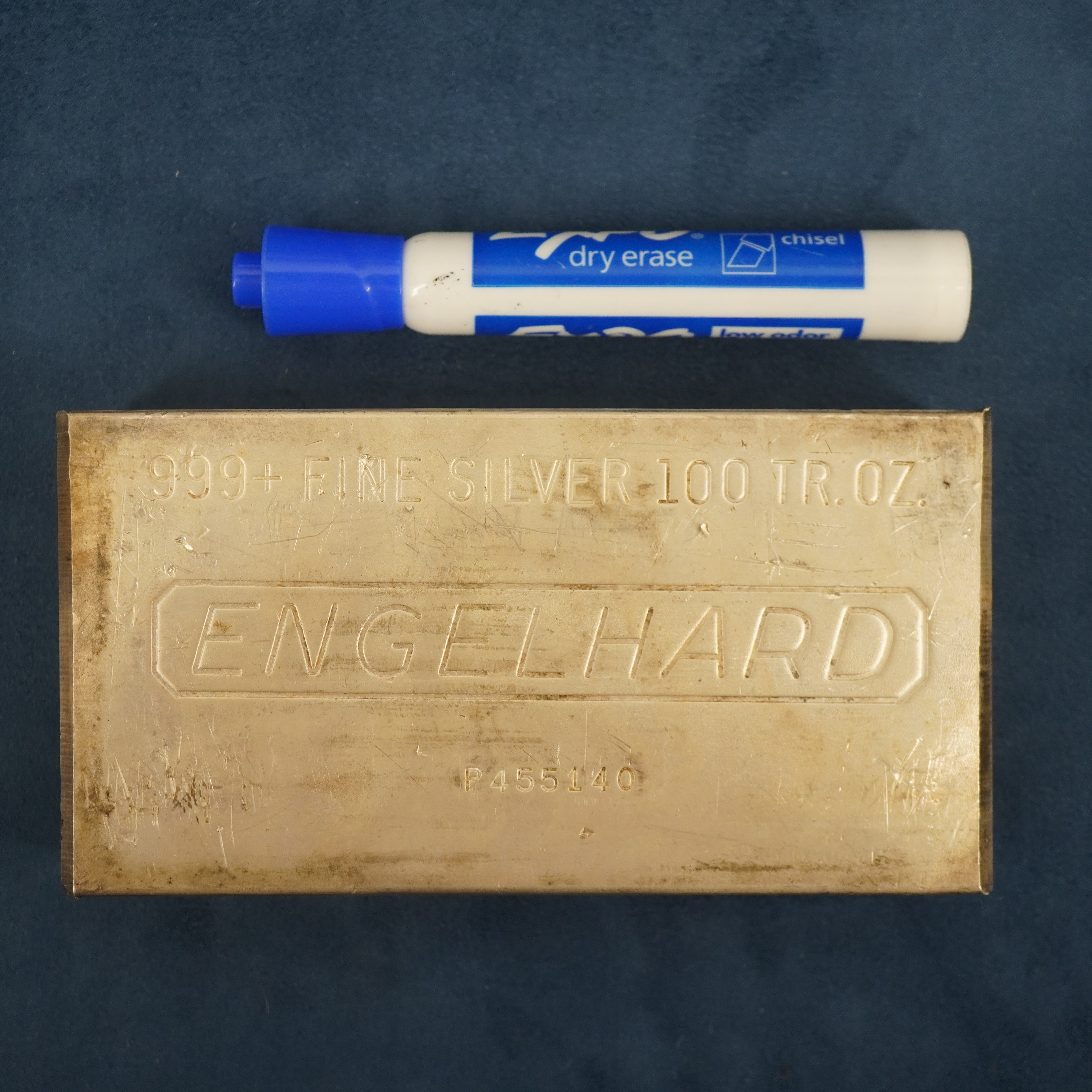 100 troy ounce bar of pure silver below an expo marker, showing that the silver bar is much bigger.