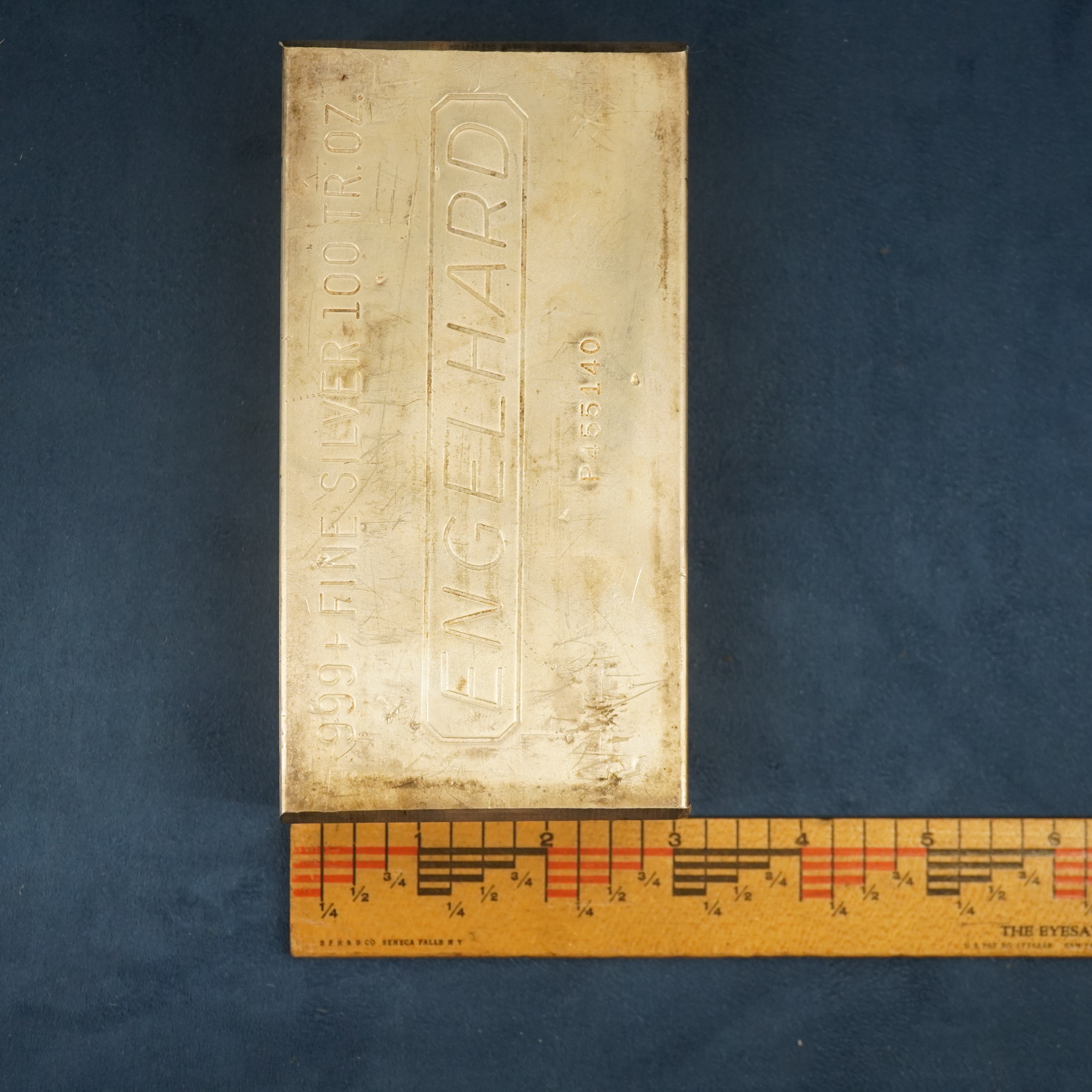 100 troy ounce pure silver bar with a ruler measuring the width of the bar to be about 3 inches.