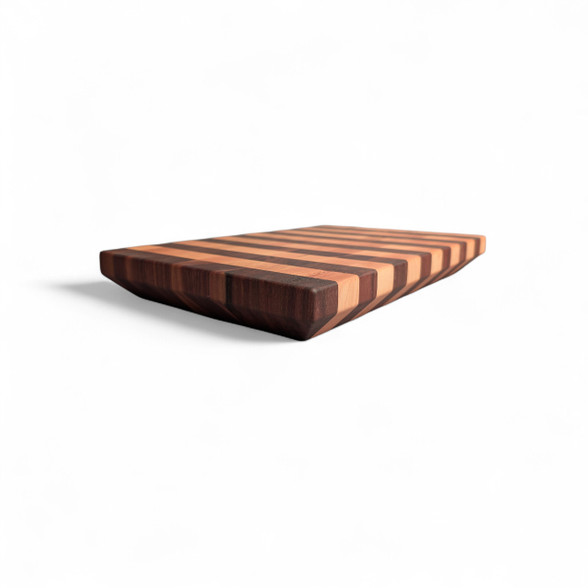 alt="Angled view of a modern end-grain cutting board with alternating stripes of Black American Walnut and Maple, featuring a 45-degree chamfered bottom edge that creates a floating effect."