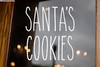 Santa's Cookies Christmas vinyl decal with tall skinny farmhouse style handwritten lettering arranged in two lines on glass window