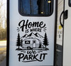 Home Is Where We Park It vinyl decal featuring a travel trailer, mountain peaks and pine trees displayed on a camper exterior