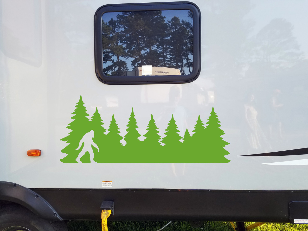 Bigfoot Sasquatch walking silhouette within a continuous pine forest tree line vinyl decal for RV campers travel trailers and trucks