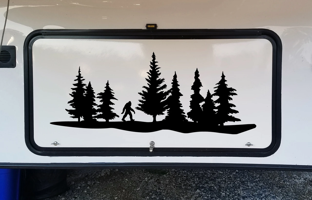 Bigfoot Sasquatch walking through pine forest tree line vinyl decal featuring evergreen trees and woodland landscape on RV camper storage compartment door