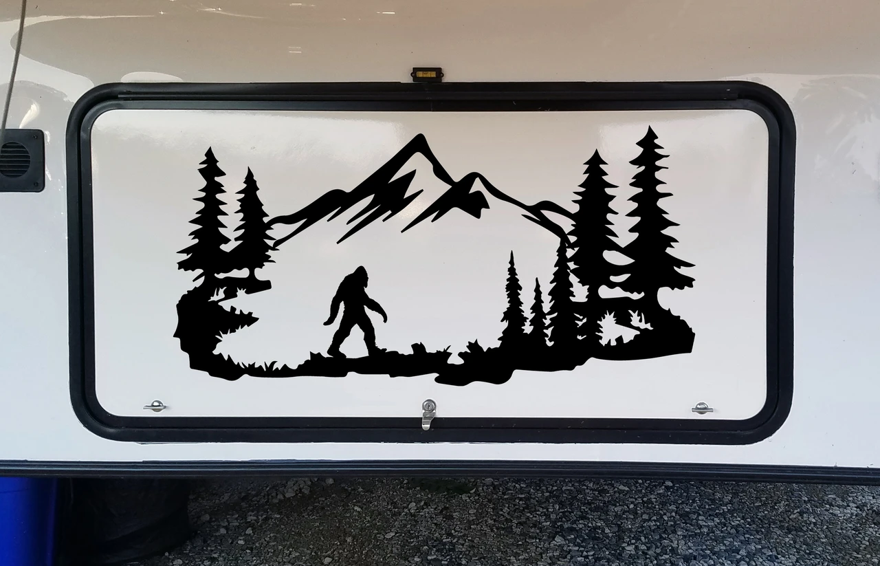 Bigfoot Sasquatch walking through mountain forest scene with evergreen pine trees and rugged peaks vinyl decal for RV camper and travel trailer