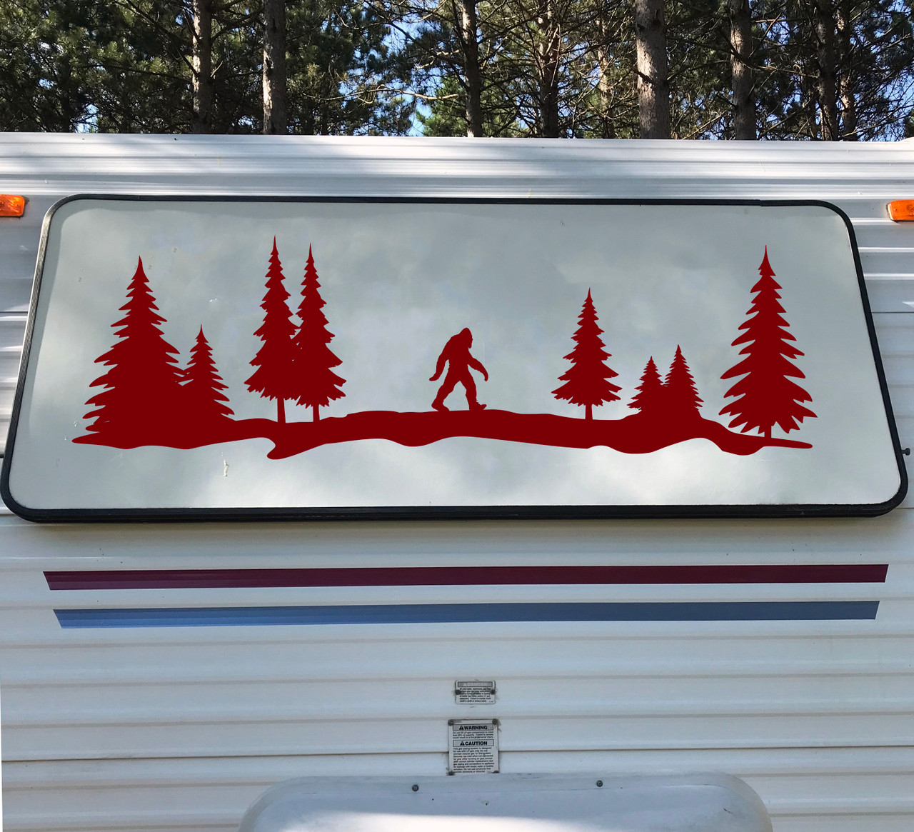 Bigfoot Sasquatch walking through a forest of tall evergreen pine trees in a wide horizontal tree line silhouette vinyl decal for RV camper and travel trailer