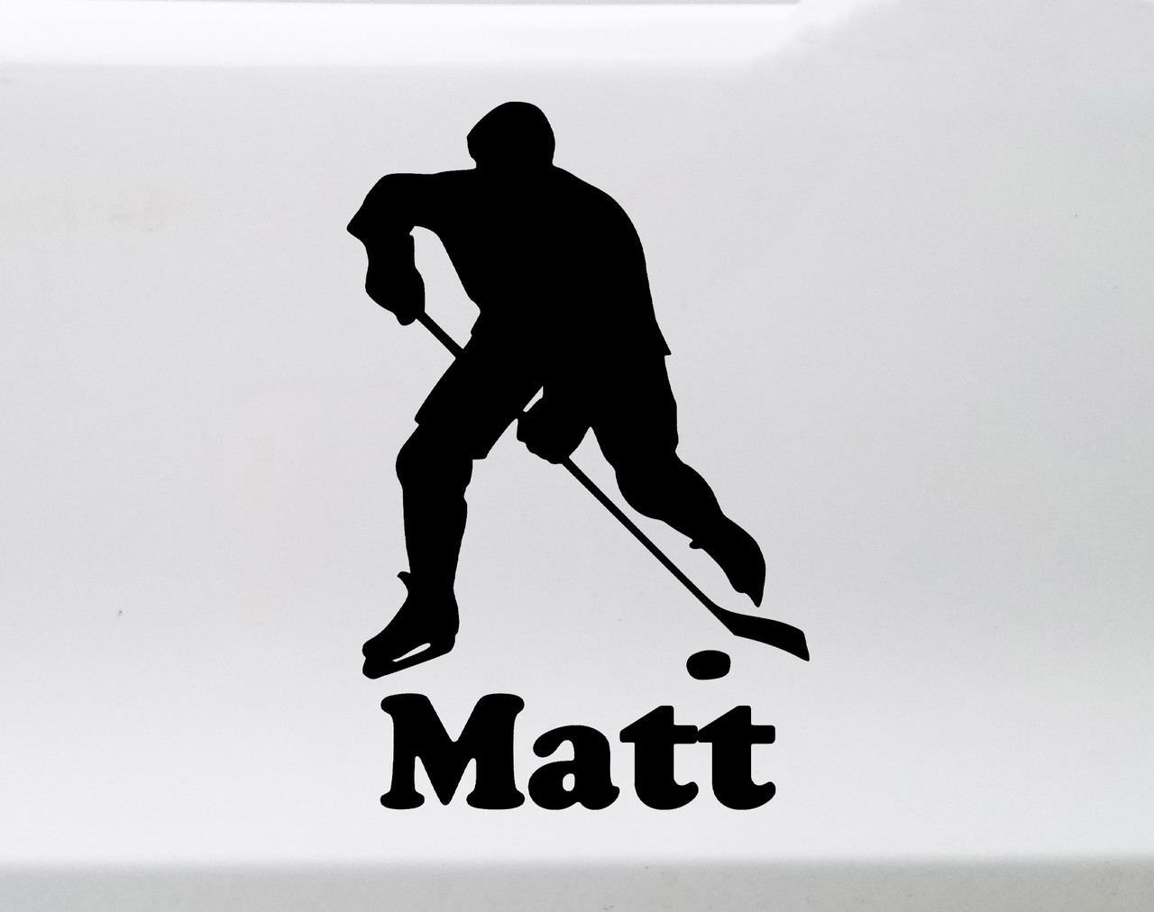 Personalized ice hockey player silhouette vinyl decal with hockey stick, puck and custom name beneath the design, available in nine sizes from 3 x 4.5 inches to 20 x 30 inches with mirror option and 12-character name personalization