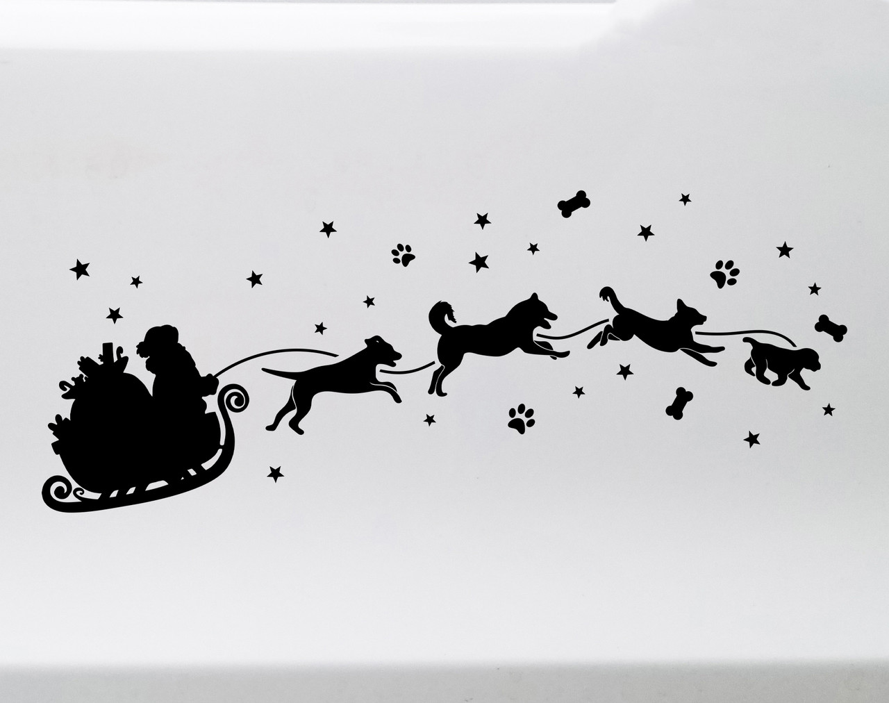 White Christmas vinyl decal of Santa Claus in a sleigh pulled by running dogs with stars, paw prints and dog bones on a glass window