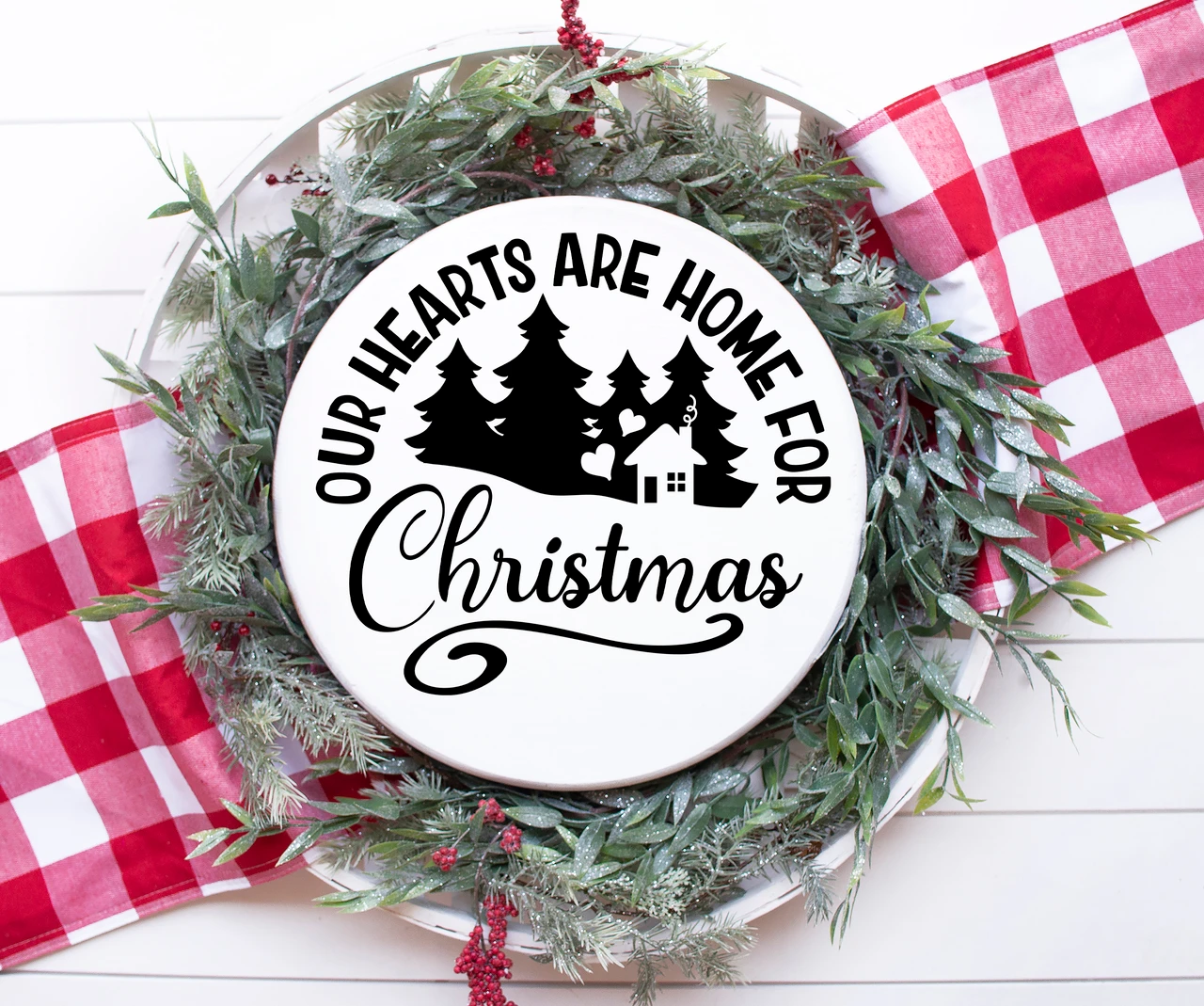 Our Hearts Are Home for Christmas vinyl window decal featuring evergreen pine trees, a small house, heart accents, arched lettering and decorative Christmas script