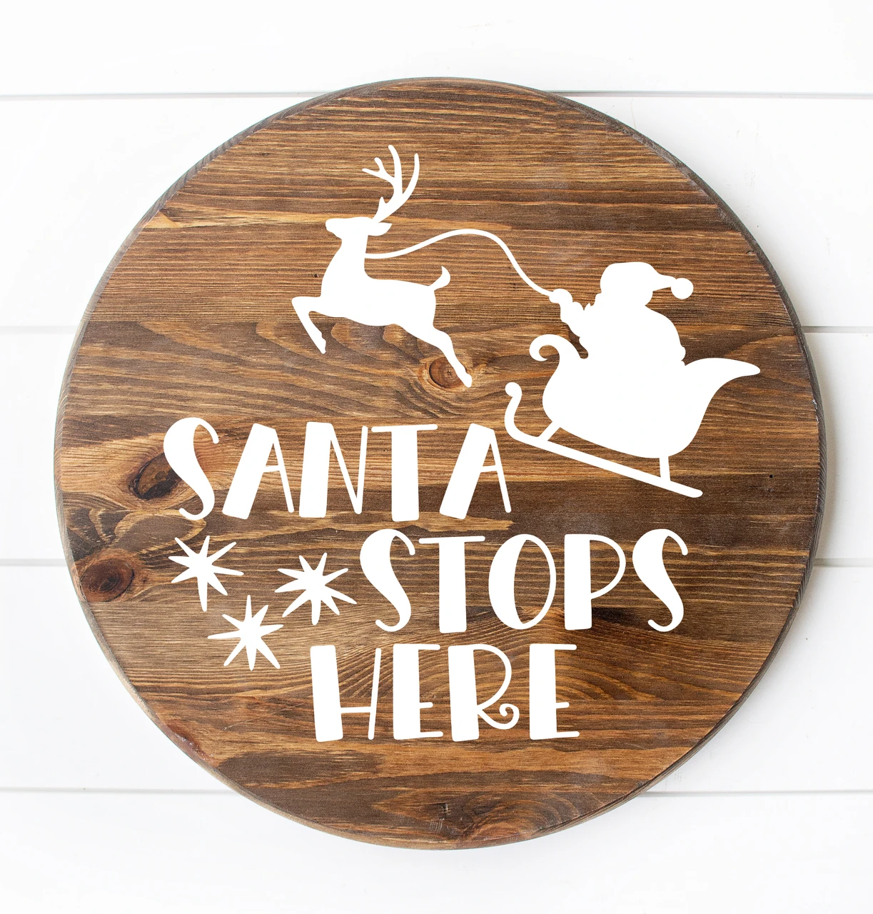 White Santa Stops Here Christmas vinyl window decal featuring Santa Claus in a sleigh pulled by a reindeer above decorative holiday lettering and stars