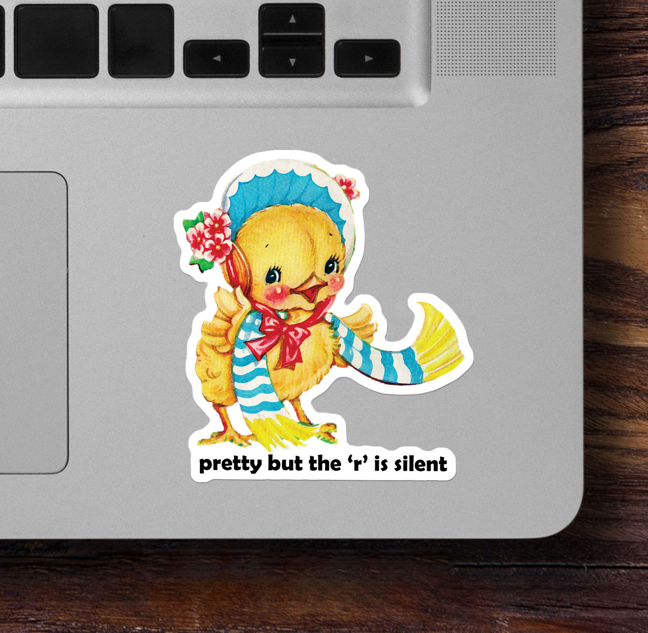 Small sarcastic vinyl sticker with text “Pretty But The R Is Silent” placed beside laptop trackpad, ideal for creative spaces