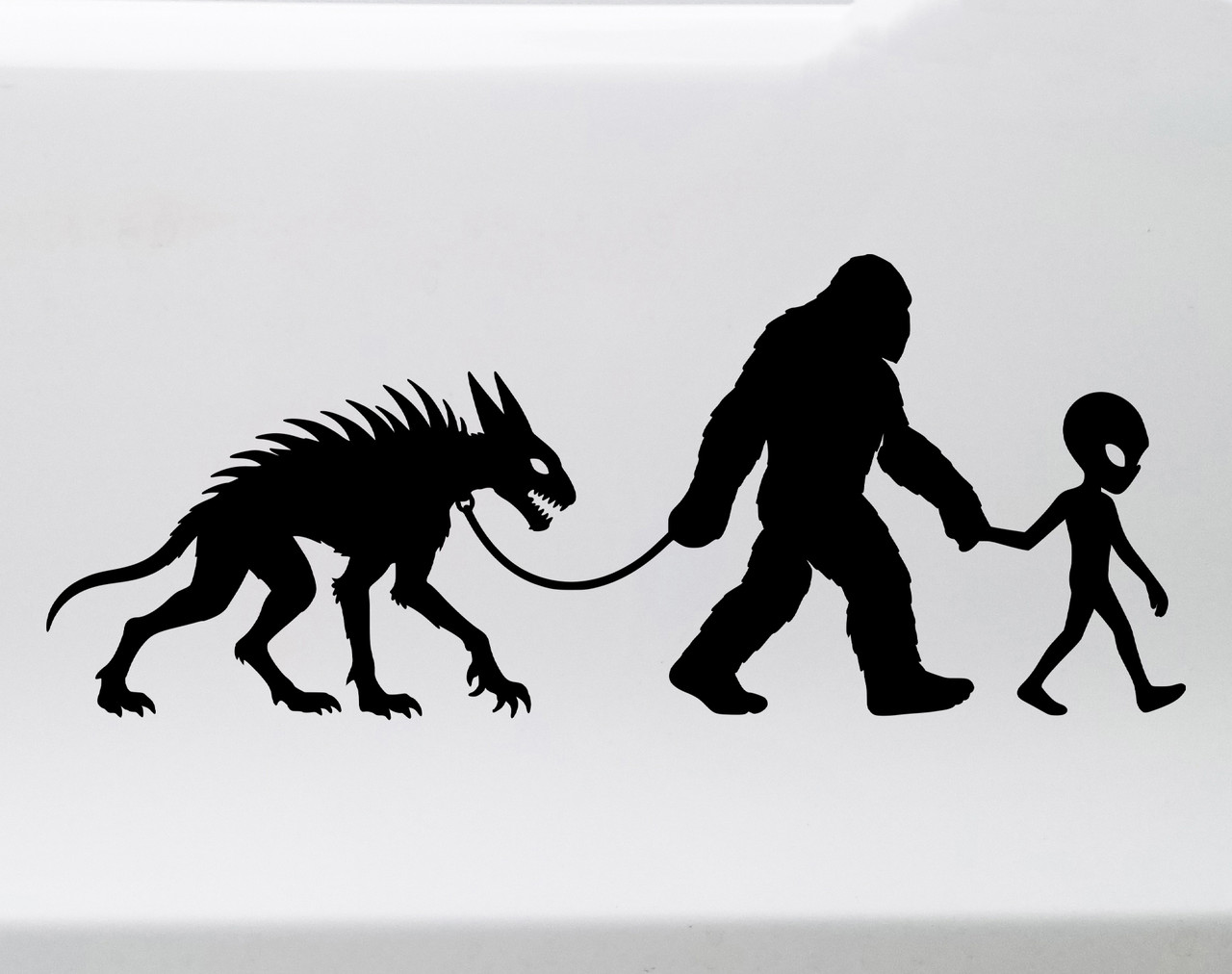 Chupacabra Bigfoot Alien Vinyl Decal Cryptid Sasquatch featuring an extraterrestrial holding hands with Bigfoot walking a leashed Chupacabra