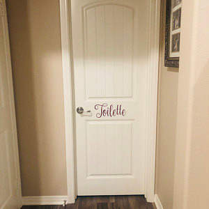 Toilette bathroom door vinyl decal featuring elegant Nouradilla script lettering with decorative flourishes, available in eight sizes from a 2-pack of 4.5 x 2 inch decals to a single 22.5 x 10 inch decal for powder rooms and restroom doors