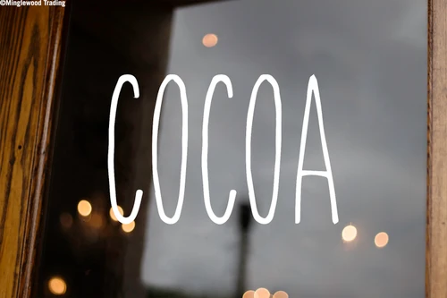 Cocoa vinyl decal featuring tall skinny farmhouse style handwritten lettering displayed on glass window for Christmas hot chocolate bar decorating